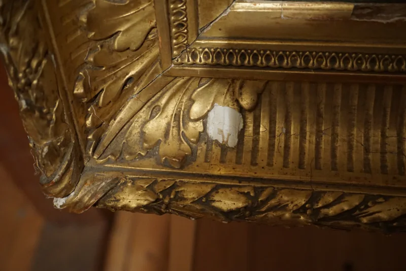 Detail of ornate gilt frame corner showing carved acanthus motif and area of gesso loss