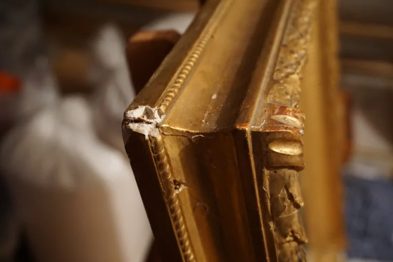 Close-up of gilt frame moulding edge showing corner damage and exposed white gesso