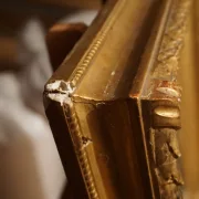 Close-up of gilt frame moulding edge showing corner damage and exposed white gesso